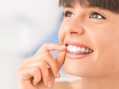 Woman with brown hair and eyes touching Invisalign over upper arch