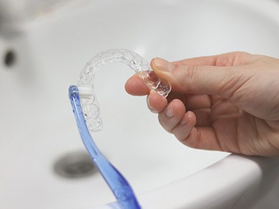 Hand holding Invisalign and scrubbing with toothbrush
