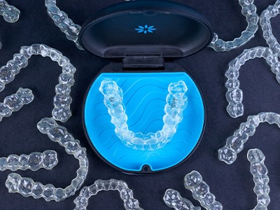 Bird’s eye view of many Invisalign trays around carrying case on black surface