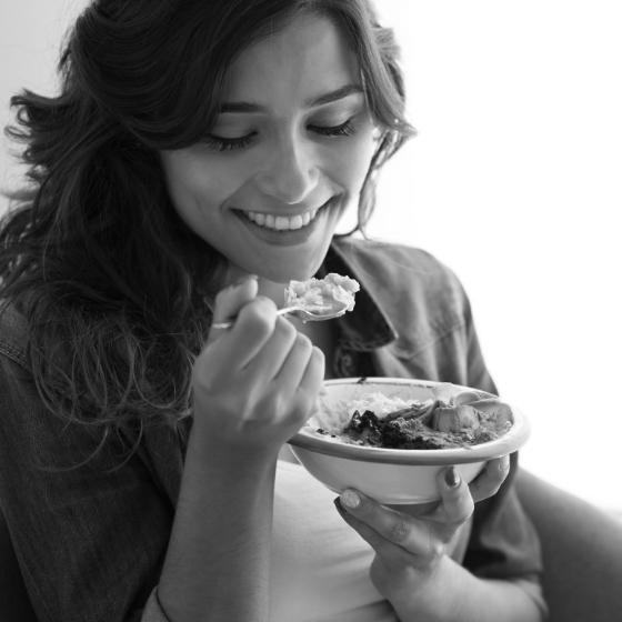 Woman smiling and holding a bowl of food with a spoon