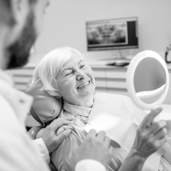 Senior dental patient holding a mirror and admiring her smile