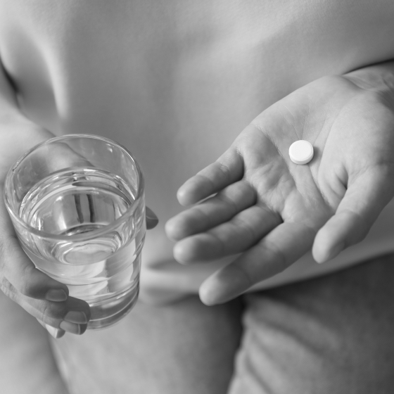 Person holding a pill in one hand and a glass of water in the other