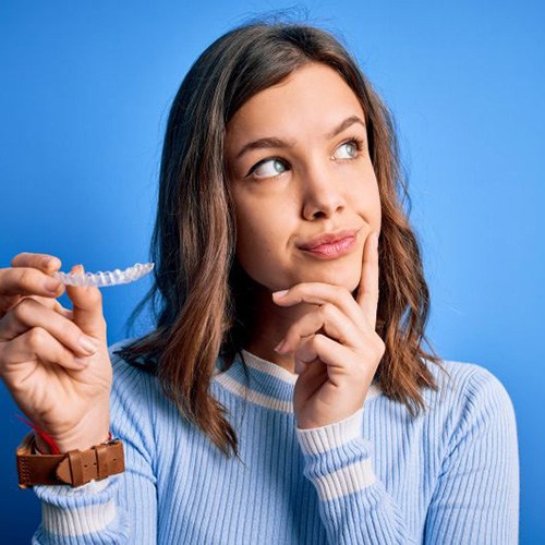 Woman holding Invisalign aligner, wearing curious expression