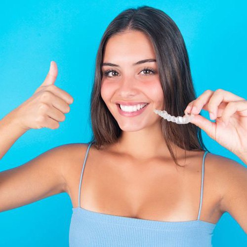 Woman holding Invisalign aligner, making thumbs-up gesture