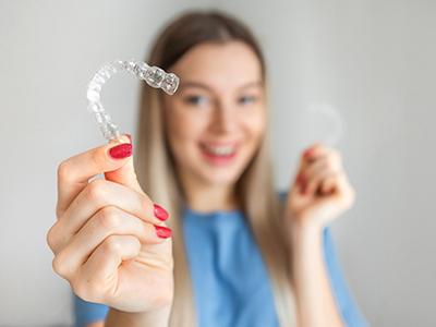Woman smiling in background holding Invisalign to foreground